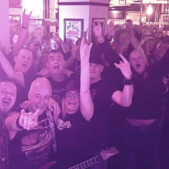 The crowd at the Pub, Lancaster, smiling, cheering and waving their arms. Guitarist Neil has also photo-bombed the picture!