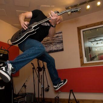 Neil jumping while playing guitar in the studio.